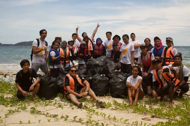 Beach cleaners stand triumphantly around bags of collected trash.
