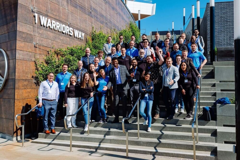 A group of people posing on outdoor stairs under a sign reading 1 Warriors Way.